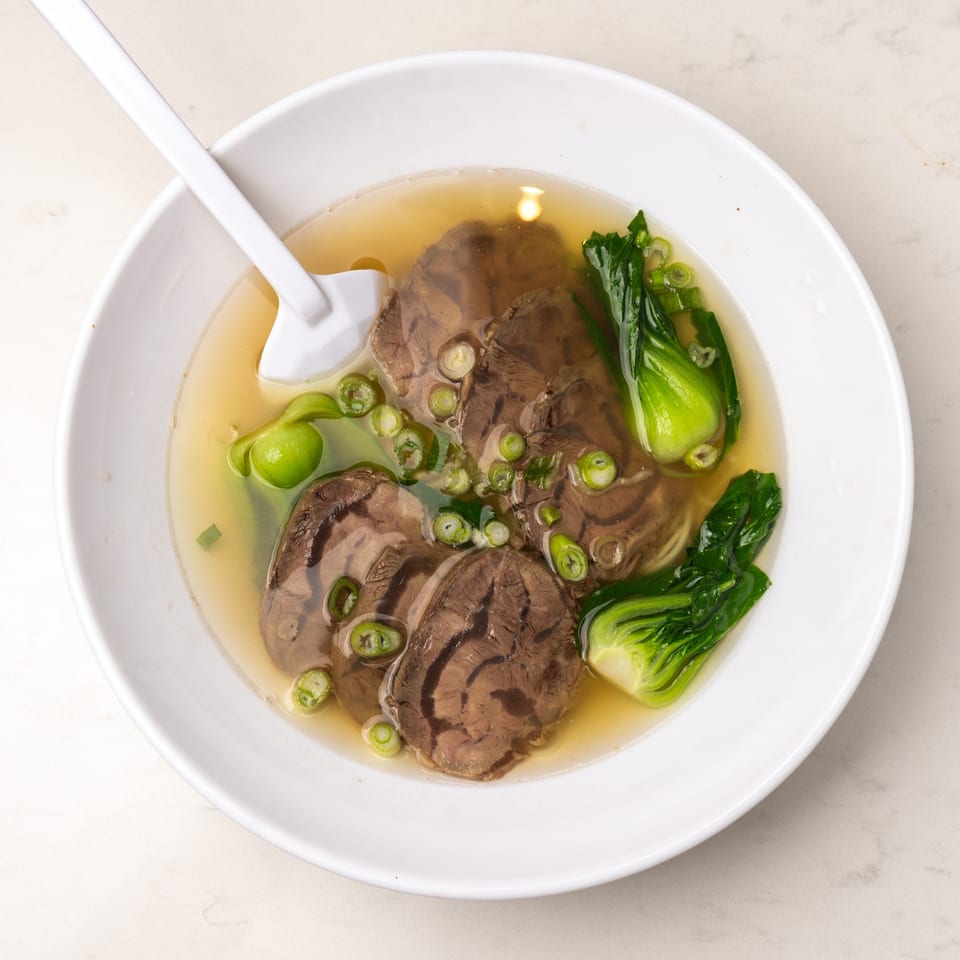 Mei Lai Xuan's beef noodle soup with bok choy and scallions in a white bowl with a spoon.