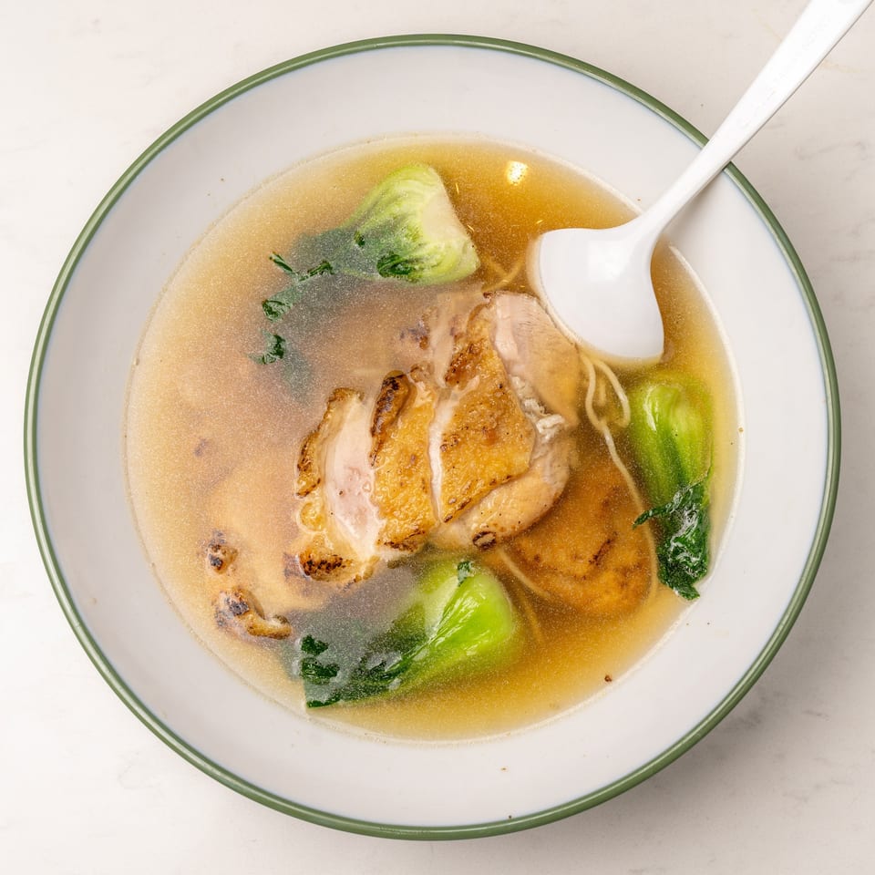 Mei Lai Xuan's chicken noodle soup with bok choy and a white spoon in a bowl.