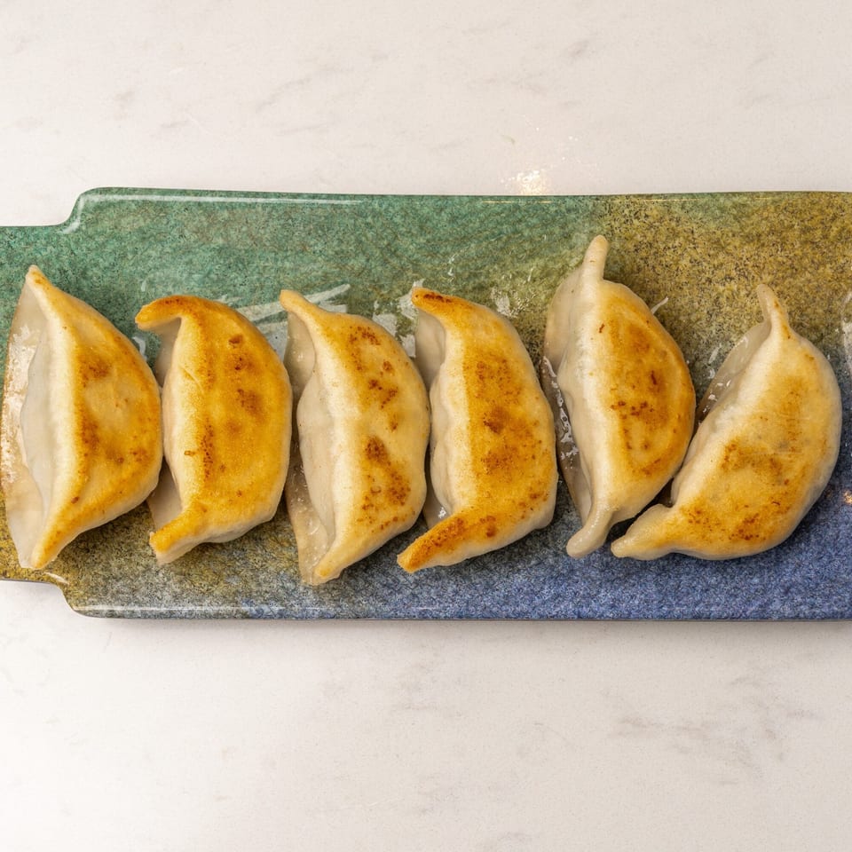 Six golden-brown pan-fried dumplings, or potstickers, arranged on a rectangular blue and green ceramic plate.