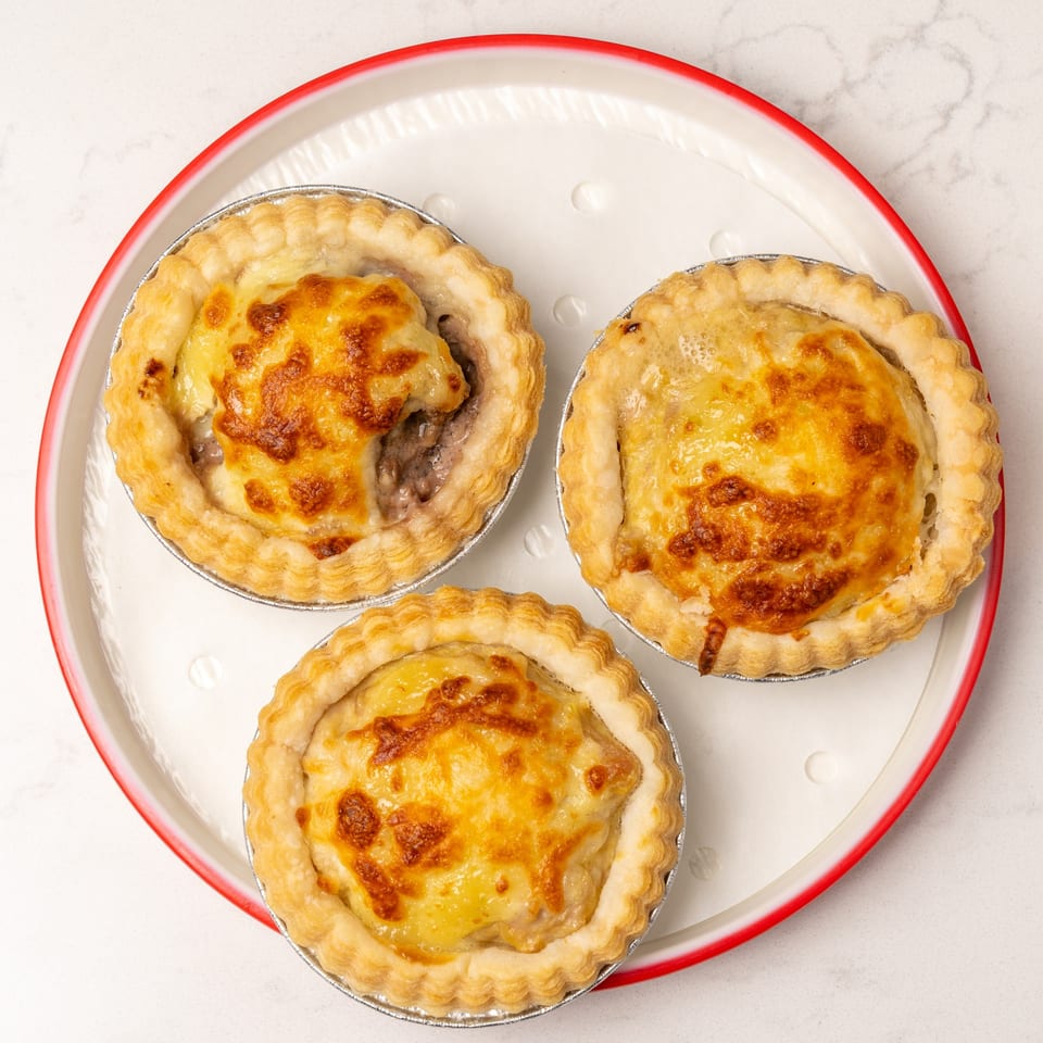 Three golden-brown baked tarts with flaky crusts and savory fillings on a white plate with a red rim.