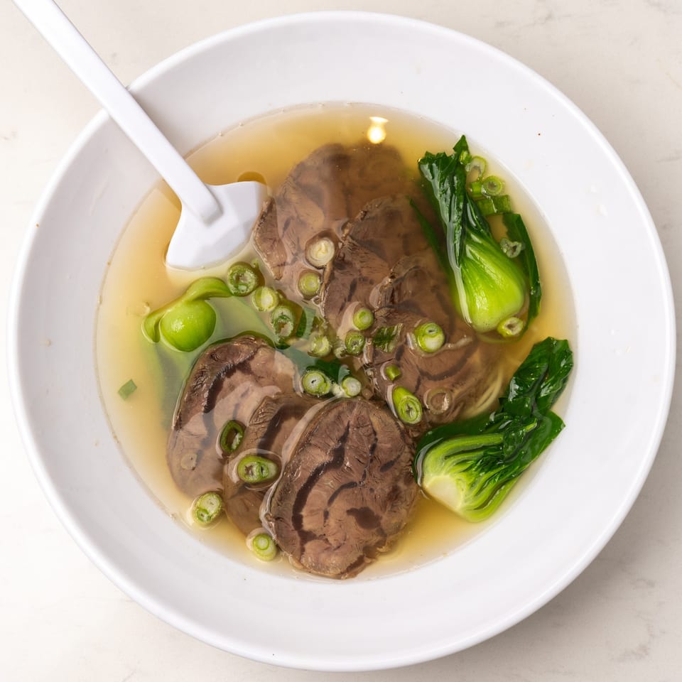 Mei Lai Xuan's beef noodle soup with bok choy and scallions in a white bowl.