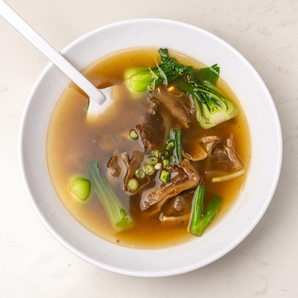 A bowl of Mei Lai Xuan Chinese soup with bok choy, mushrooms, and green onions.