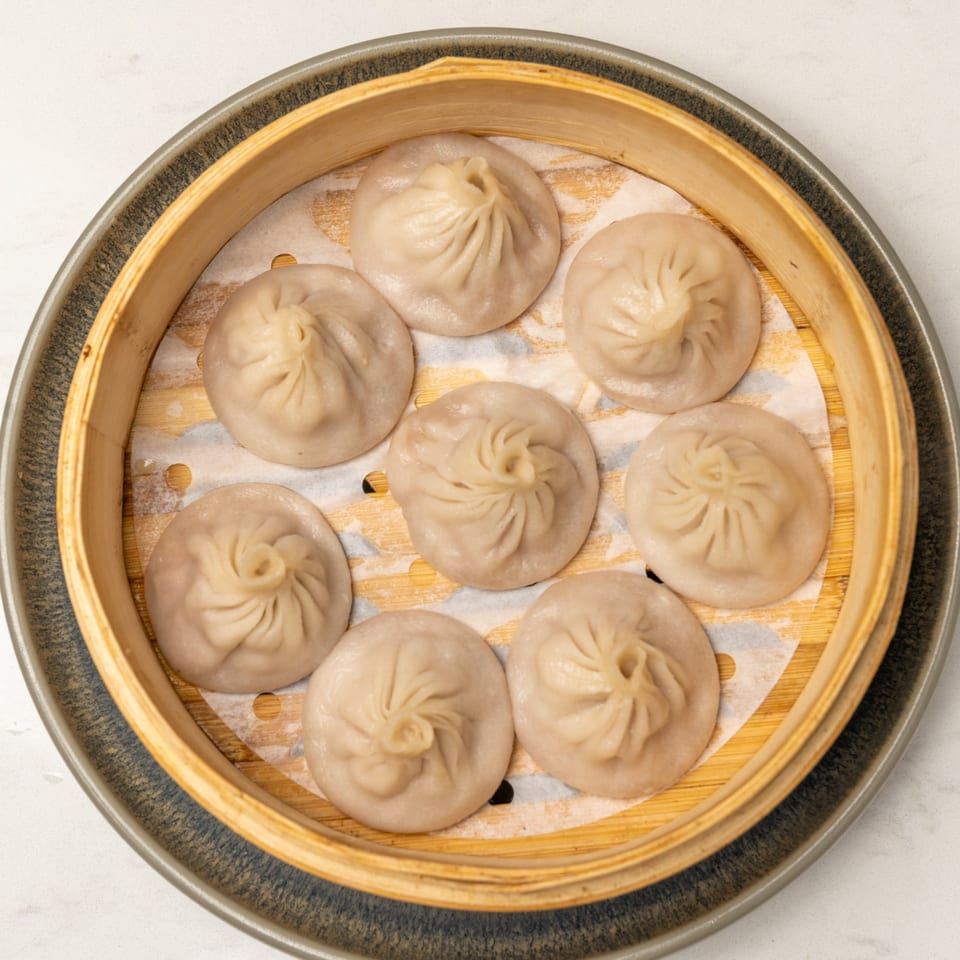 Eight steamed Mei Lai Xuan soup dumplings (xiao long bao) in a bamboo steamer basket.